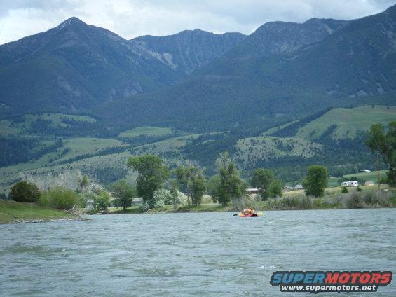 Kayak on a wide river with rolling hills and mountains behind it