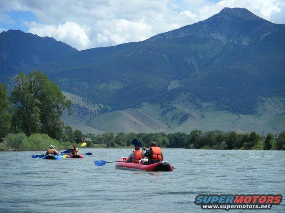 Kayaks on a river with mountains in the background. Water is choppy