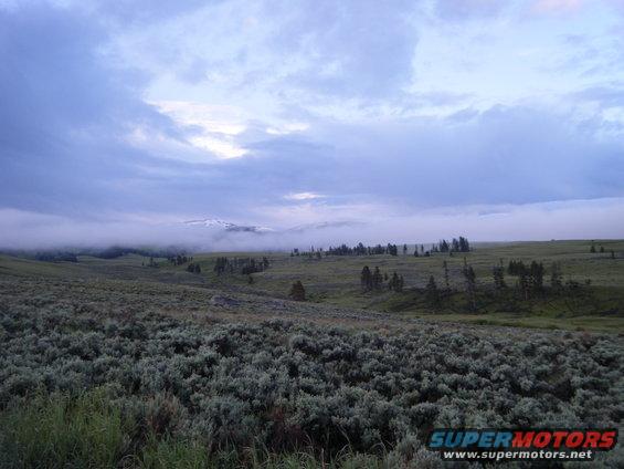 Mountain landscape with low clouds and scattered trees over rolling hills