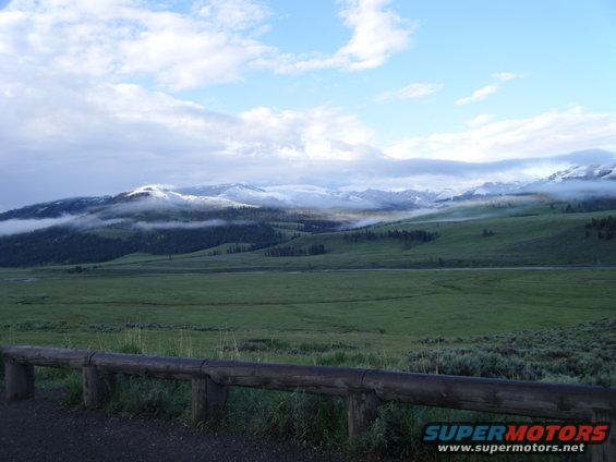 Mountain landscape with green hills, snow-capped peaks, and clouds