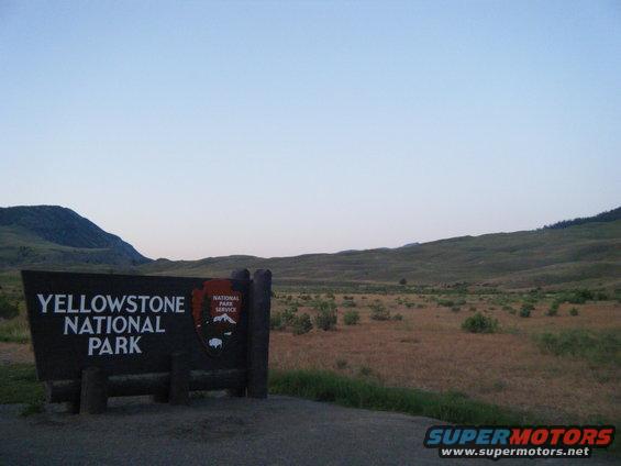 Yellowstone National Park sign with mountains and dry grass landscape