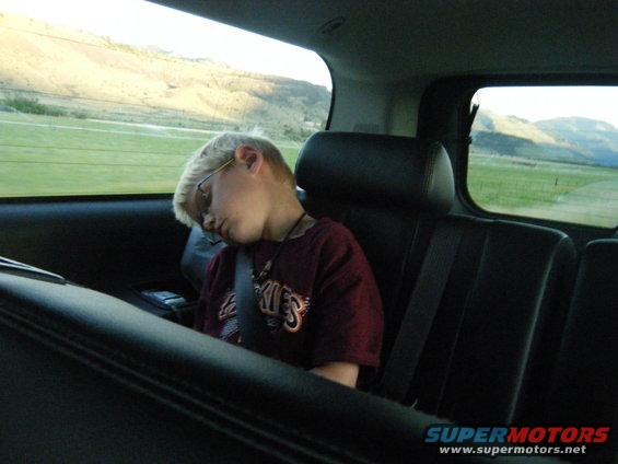 Child wearing glasses and a maroon shirt sleeps in the back seat of a vehicle