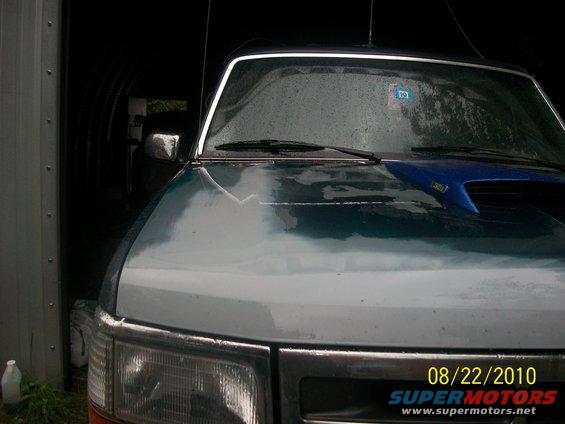 Front of a 1990s Ford truck, possibly a Bronco, in a garage. Blue hood scoop visible