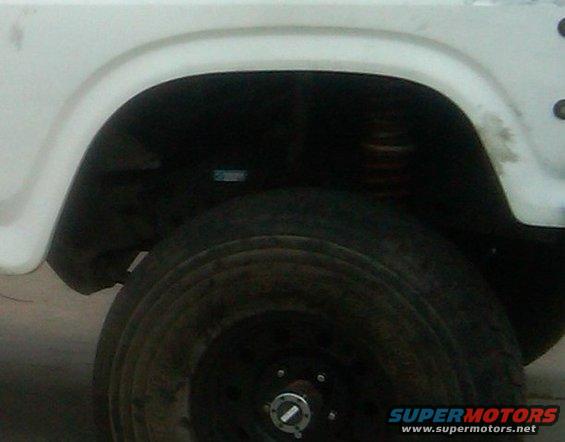 White vehicle's rear wheel well and tire, showing suspension and part of the body panel