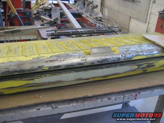 Yellow tailgate with peeling paint and exposed metal, resting on a workbench