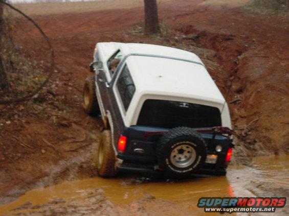 Rear view of a 1986 Ford Bronco driving through mud with a spare tire mounted