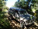 1992 Ford Bronco - A dusty Ford Bronco navigates a wooded trail under a clear blue sky.