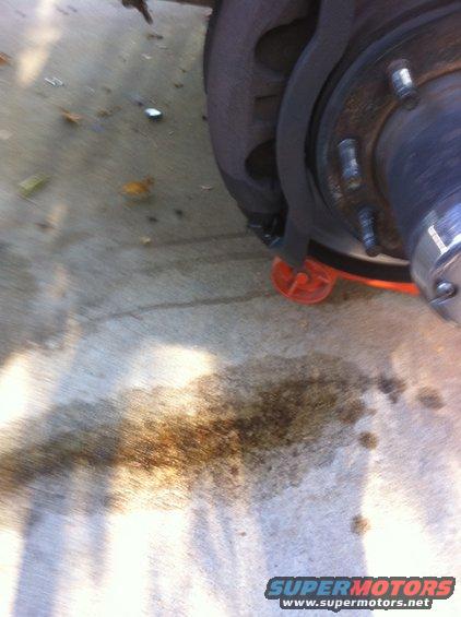 Close-up of a vehicle's brake rotor and caliper with fluid stains on the ground