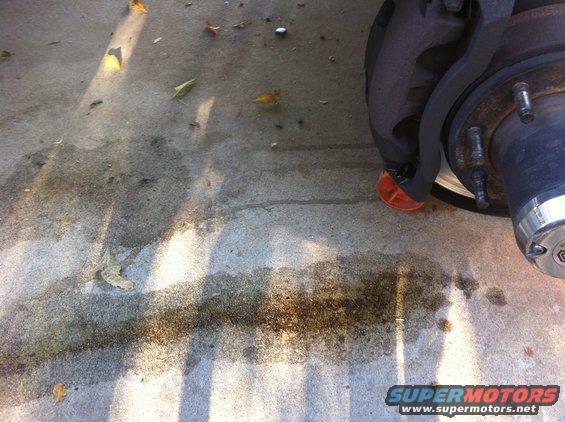 Truck brake caliper and rotor with orange chock on concrete with oil stains