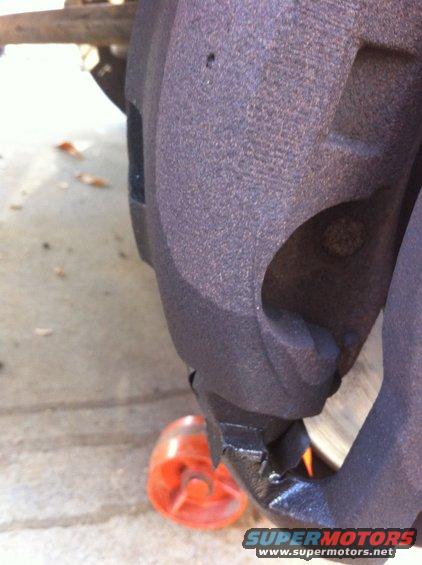 Close-up of a rusty brake caliper with an orange wheel chock nearby