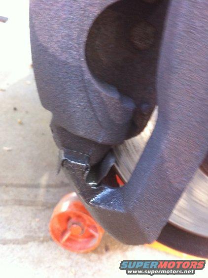 Close-up of a black brake caliper over a rotor, with an orange plastic chock visible
