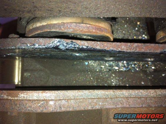 Close-up of rusted metal with weld marks and debris, showing Supermotors.net logo