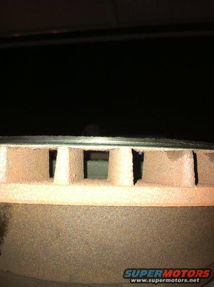 Close-up of a rusty, vented brake rotor with square holes