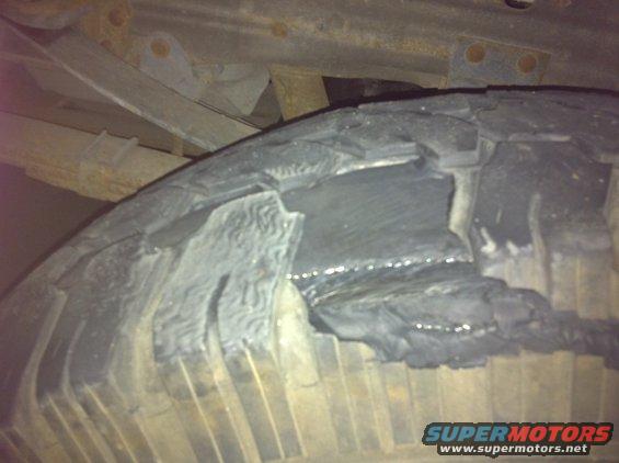 Damaged tire with exposed inner layers and visible rust on suspension components