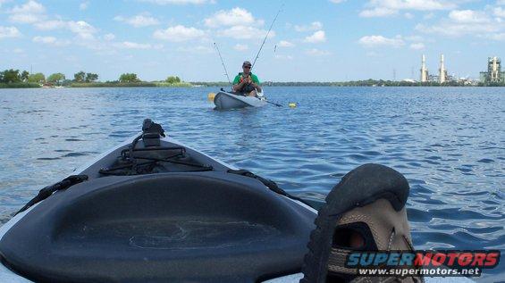 Two kayaks on a blue lake under a cloudy sky, one in the foreground and one with a fisherman in the distance