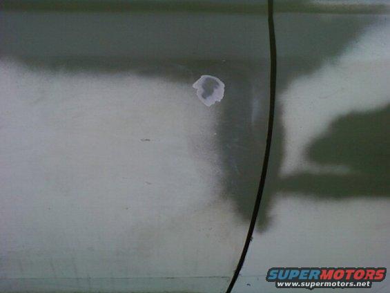 close-up of a vehicle's body panel with primer and a small patch of filler