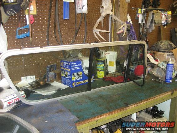 Car window frame and glass on a workbench with tools and parts in the background