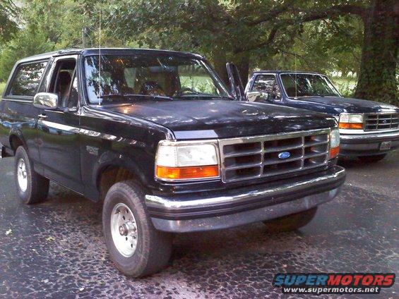 Black Ford Bronco with open driver door, parked on asphalt driveway next to another SUV