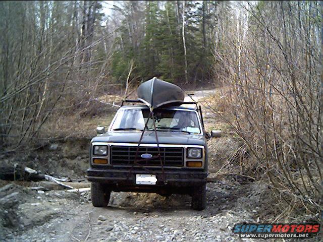 Dark green Ford Bronco with a canoe on its roof rack, driving on a dirt road