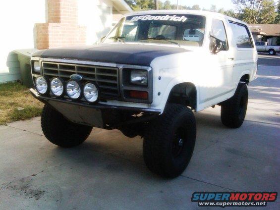White Ford Bronco with BFGoodrich sticker on windshield, aftermarket bumper, and four fog lights mounted on the front