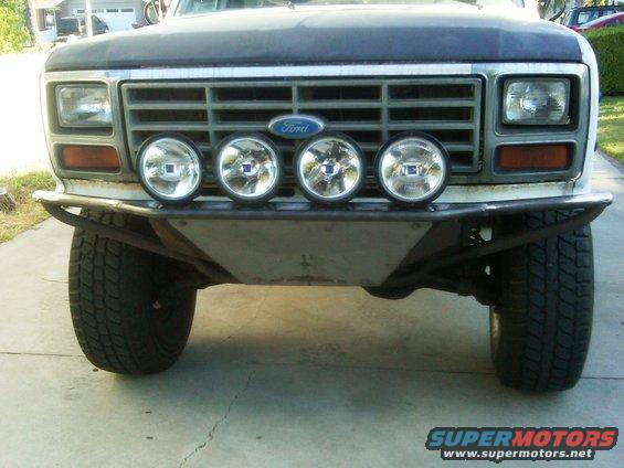 Front view of a Ford Bronco with a custom bumper and four driving lights mounted above it. The grille has a Ford logo