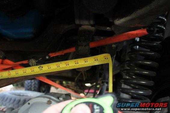 Measuring suspension components with a yellow tape measure, showing a coil spring and red strap
