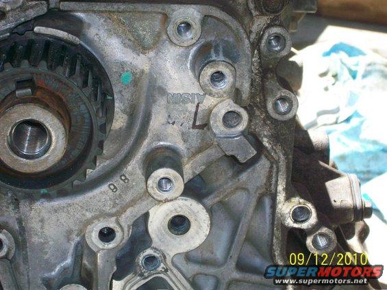 Close-up of an engine block with gears and bolts visible. Text 'AISIN' is stamped on the metal