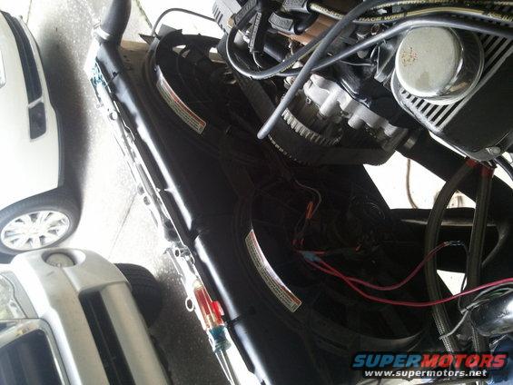 Engine bay with electric fan and wiring. Part of a white vehicle and silver SUV visible