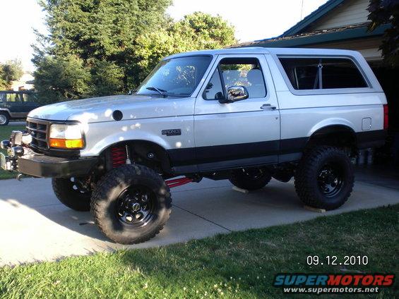 Silver lifted Ford Bronco with aftermarket bumper and large tires, parked on a driveway