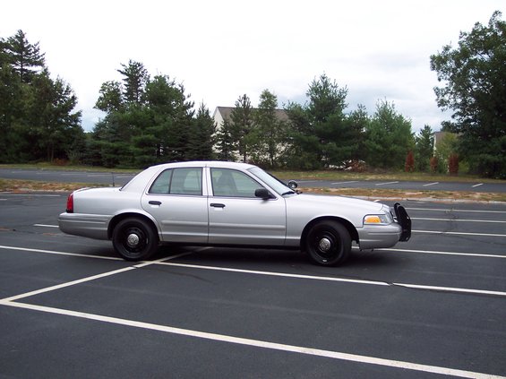 Silver 2001 Ford Crown Victoria police car, side view, parked in an empty lot