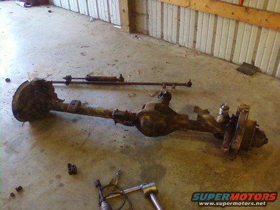 Front axle assembly with steering linkage removed, sitting on a concrete floor