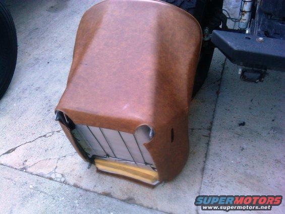 Brown vinyl car seat with exposed foam and metal frame, resting on concrete