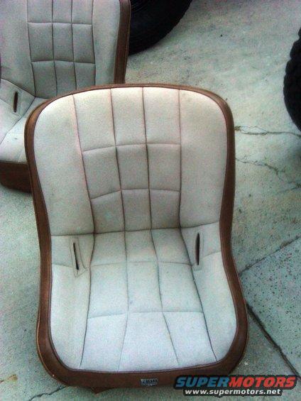 Two bucket car seats with light-colored upholstery and brown trim. One seat is in focus in the foreground