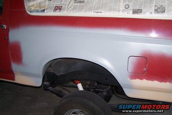 Side view of vehicle body with primer and red paint, undergoing prep work