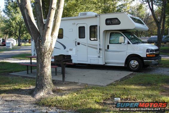 White RV parked at campsite with picnic table and grill