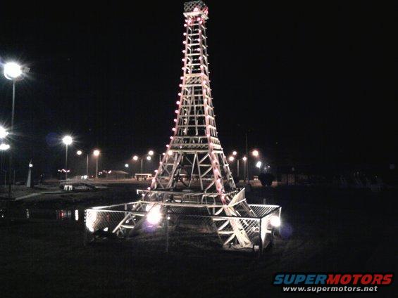 Eiffel Tower replica illuminated at night with lights and a fence around its base