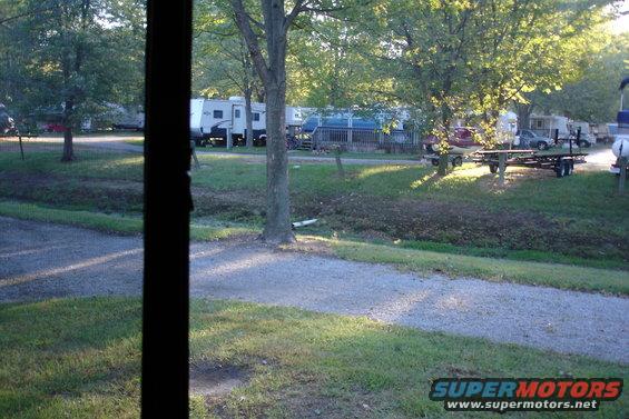 RV park with several campers and trailers parked, trees and grass visible