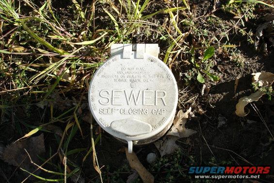 White sewer cap with text 'SEWER SELF-CLOSING CAP' on the ground