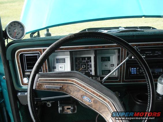 Dashboard of a 1979 Ford F-150 with wood grain trim, gauges, and a steering wheel. A tachometer is mounted on the dash