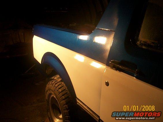 Side view of a two-tone blue and white Ford Bronco, showing the rear quarter panel and tire