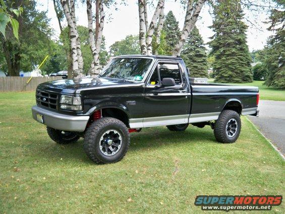 Black 1995 Ford F-150 pickup truck with lifted suspension and aftermarket wheels parked on grass