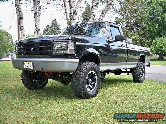 Lifted black Ford F-150 pickup truck parked on grass with trees in the background