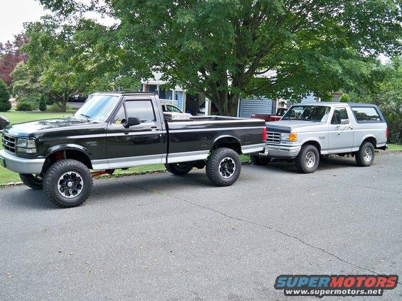 Black Ford F-150 pickup truck and silver Ford Bronco parked on a residential street