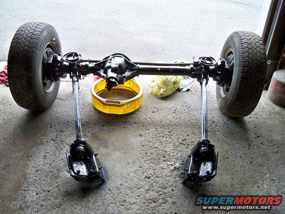 Rear axle assembly with two wheels, a yellow oil drain pan, and a yellow plastic bag on concrete