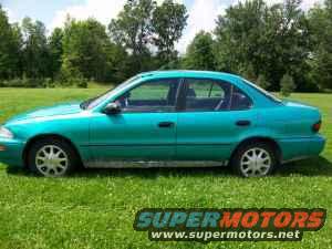 1994 Geo Prizm sedan, teal green, parked on grass with trees in background
