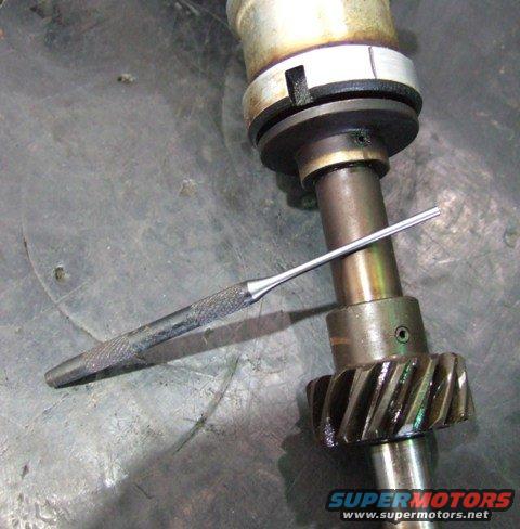 Close-up of a distributor shaft with a gear and a small tool resting on it