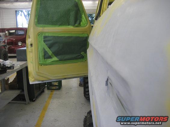 Yellow vehicle door and fender with masking tape, another red vehicle in background