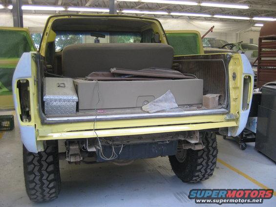 Rear view of a yellow 1978 Ford Bronco with its tailgate open, showing interior storage and parts
