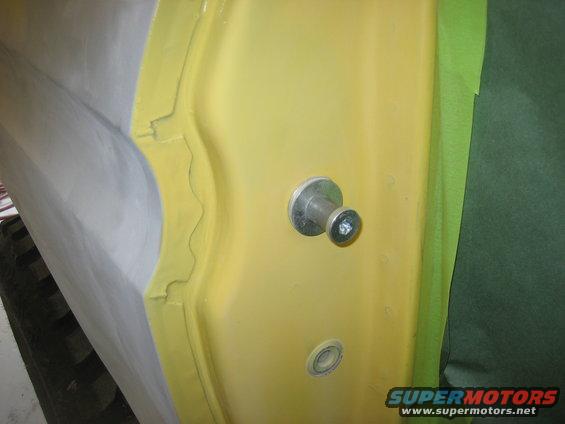 Close-up of a yellow car door interior panel with a silver knob and screw, and green masking tape on the edge
