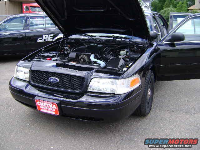 Black 2003 Ford Crown Victoria, hood open showing engine. Another black car with 'CRE' visible is in the background